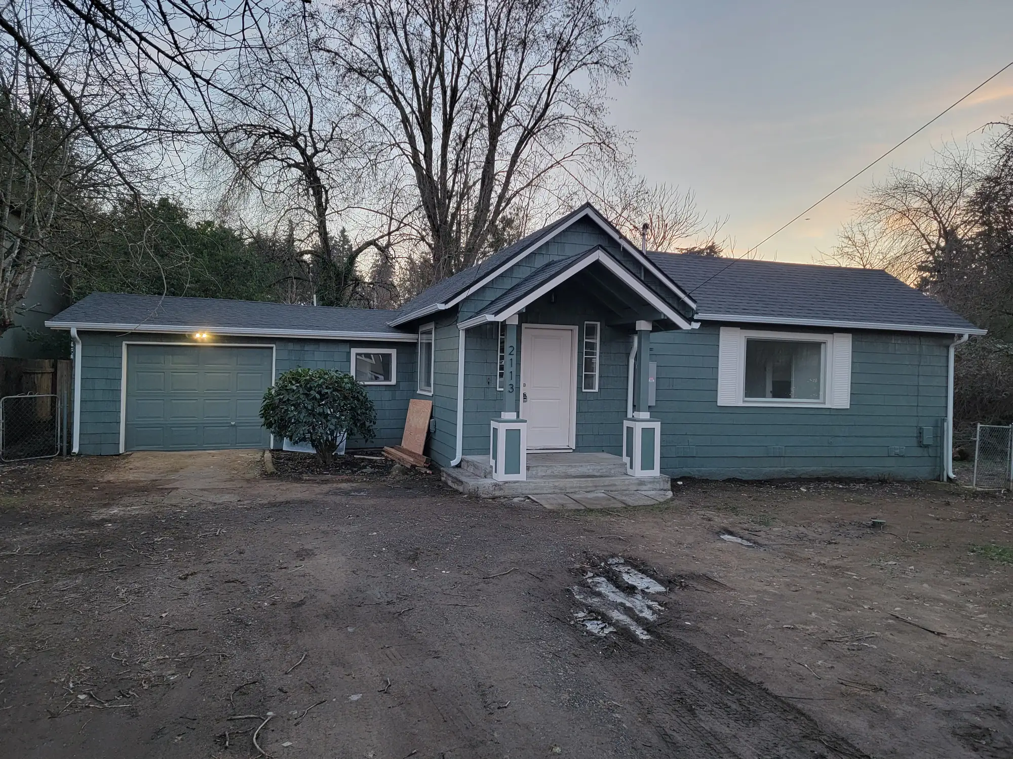 Done: Front exterior at dusk — paint and roof done, drive still gravel.