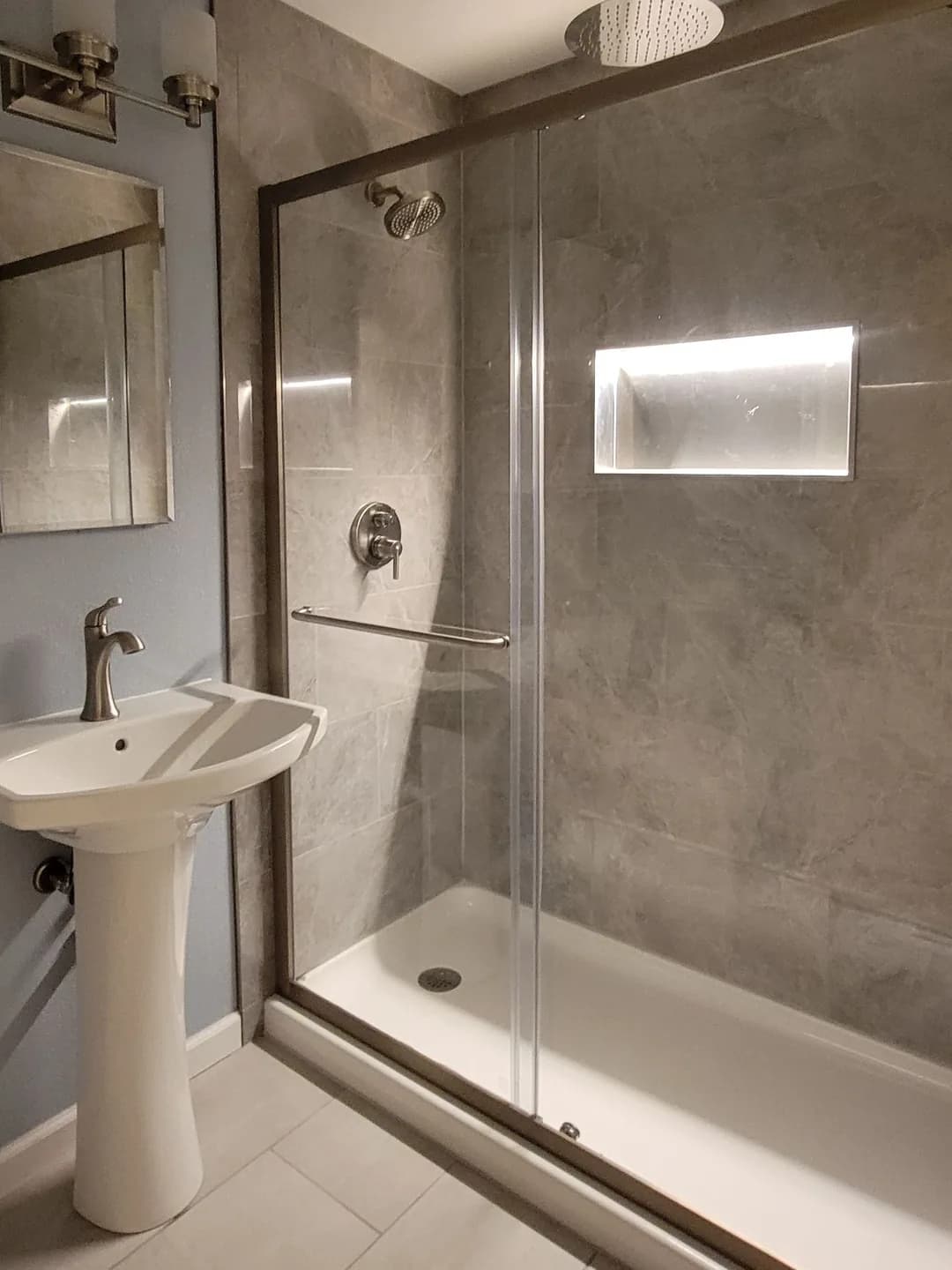 Finished NE 12th St bathroom: tiled walk-in shower with rain head, lit niche and sliding glass door